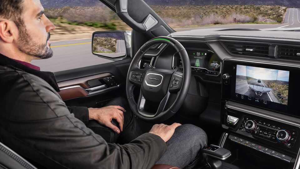Profile View of a Man Using Super Cruise in his GMC While the Infotainment Screen Displays the Transparent Trailer View