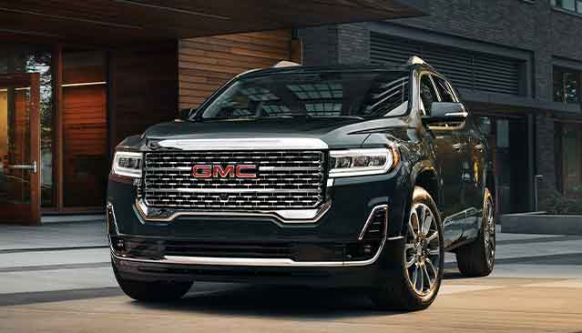 A Dark Colored GMC Acadia SUV Parked in Front of a Modern Building With Wooden Accents