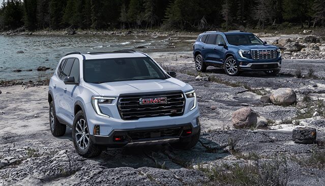 Two GMC Terrain SUVs, One Light Gray and One Blue, Parked on a Rocky Shore by a Lake