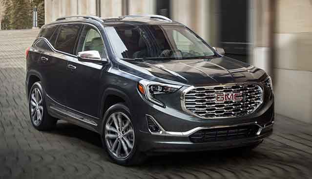 A Dark Gray GMC Terrain SUV Driving on a City Street With Blurred Buildings in the Background