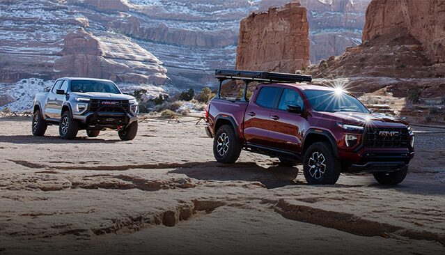 A Gray GMC Canyon AT4X and a Red GMC Canyon AT4X AEV Edition Pickup Truck Parked on a Rocky Desert Landscape