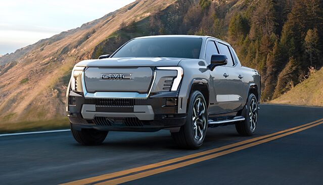 A Light Gray GMC Sierra EV Pickup Truck Driving on a Winding Mountain Road