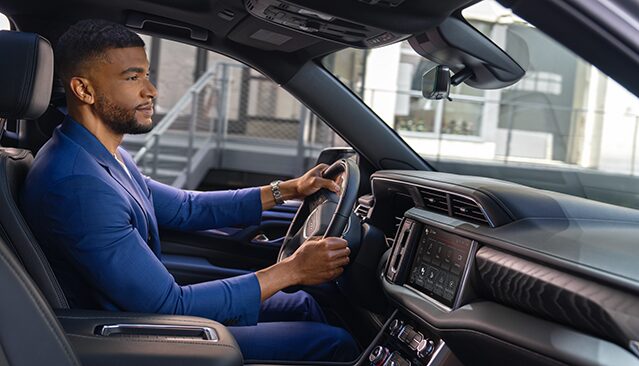 A Man in a Blue Suit Driving a GMC Truck, Seen from the Passenger Side, with an Upscale Urban Building in the Background