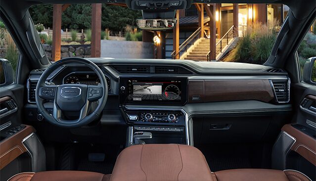 The Interior View of a GMC Truck Dashboard and Steering Wheel, Featuring Brown Leather and Modern Infotainment Screens