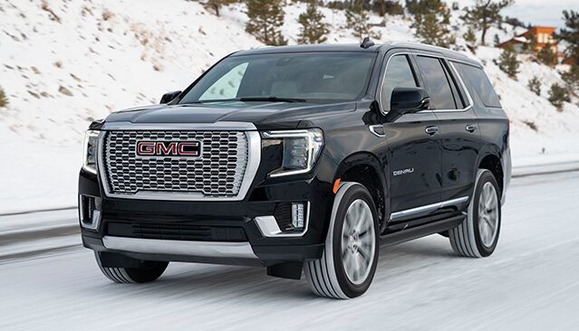 A Black GMC Yukon Denali SUV Driving on a Snow-Covered Road With Pine Trees in the Background
