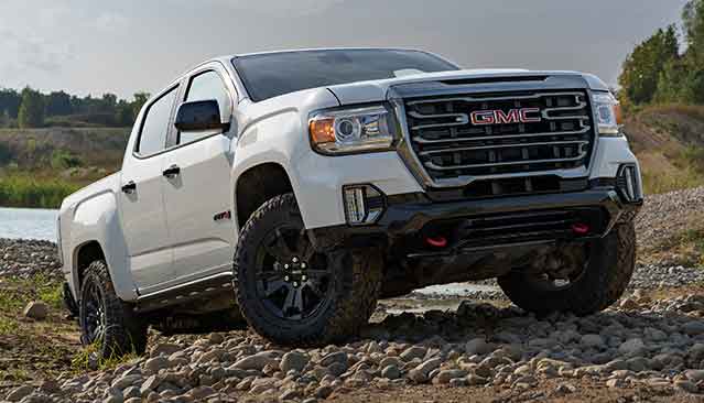 A White GMC Canyon Pickup Truck With Off-Road Tires Parked on a Rocky Terrain Near Water