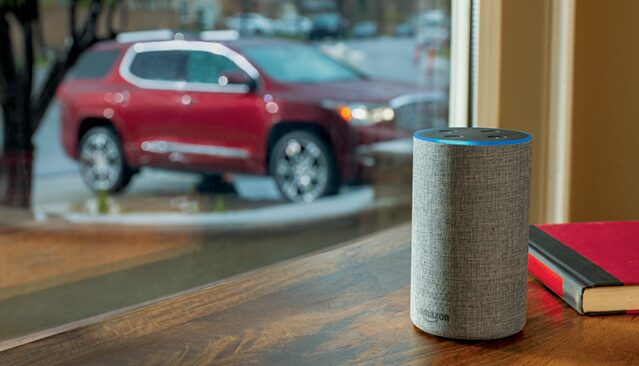 An Amazon Echo Speaker on a Table Indoors With a Red GMC Acadia SUV Visible Through a Window Outside