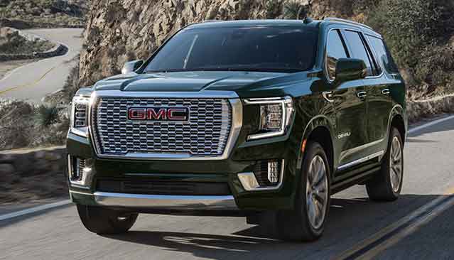 A Dark Green GMC Yukon Denali SUV Driving on a Winding Road Through a Mountainous Landscape