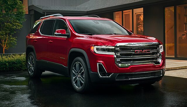 A Red GMC Acadia Parked Outside a Modern House on Wet Pavement with a Sleek Design
