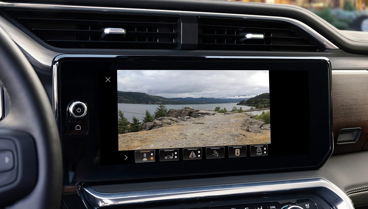 GMC Infotainment Screen Showing a High-Definition Rear Camera View of a Scenic Lake with Mountains and Trees