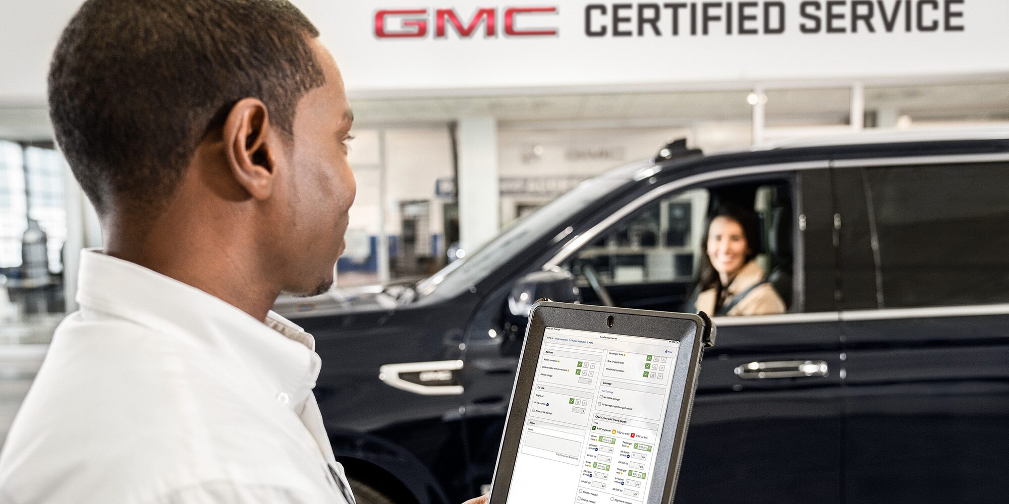 GMC Certified Service Representative Holding a Tablet Smiling at a Customer Sitting in Their Vehicle