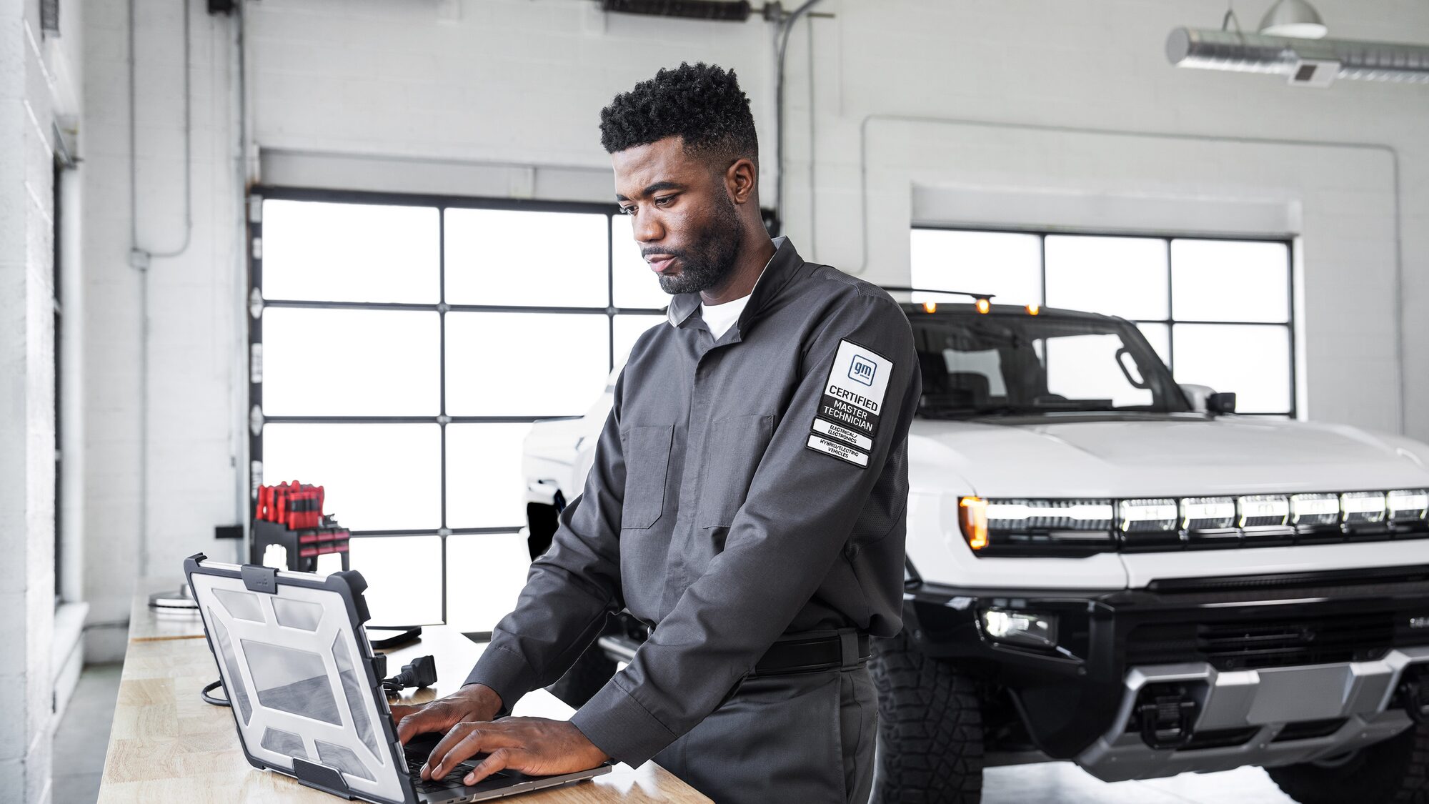 GMC Certified Technician Using a Laptop for Vehicle Diagnostics in a Well-Lit Garage