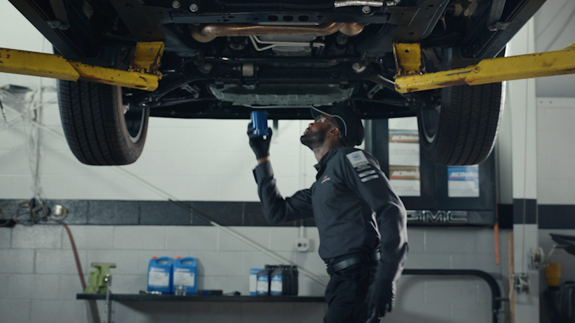 A GMC Service Technician Looking Under a Lifted Vehicle in a Service Garage.