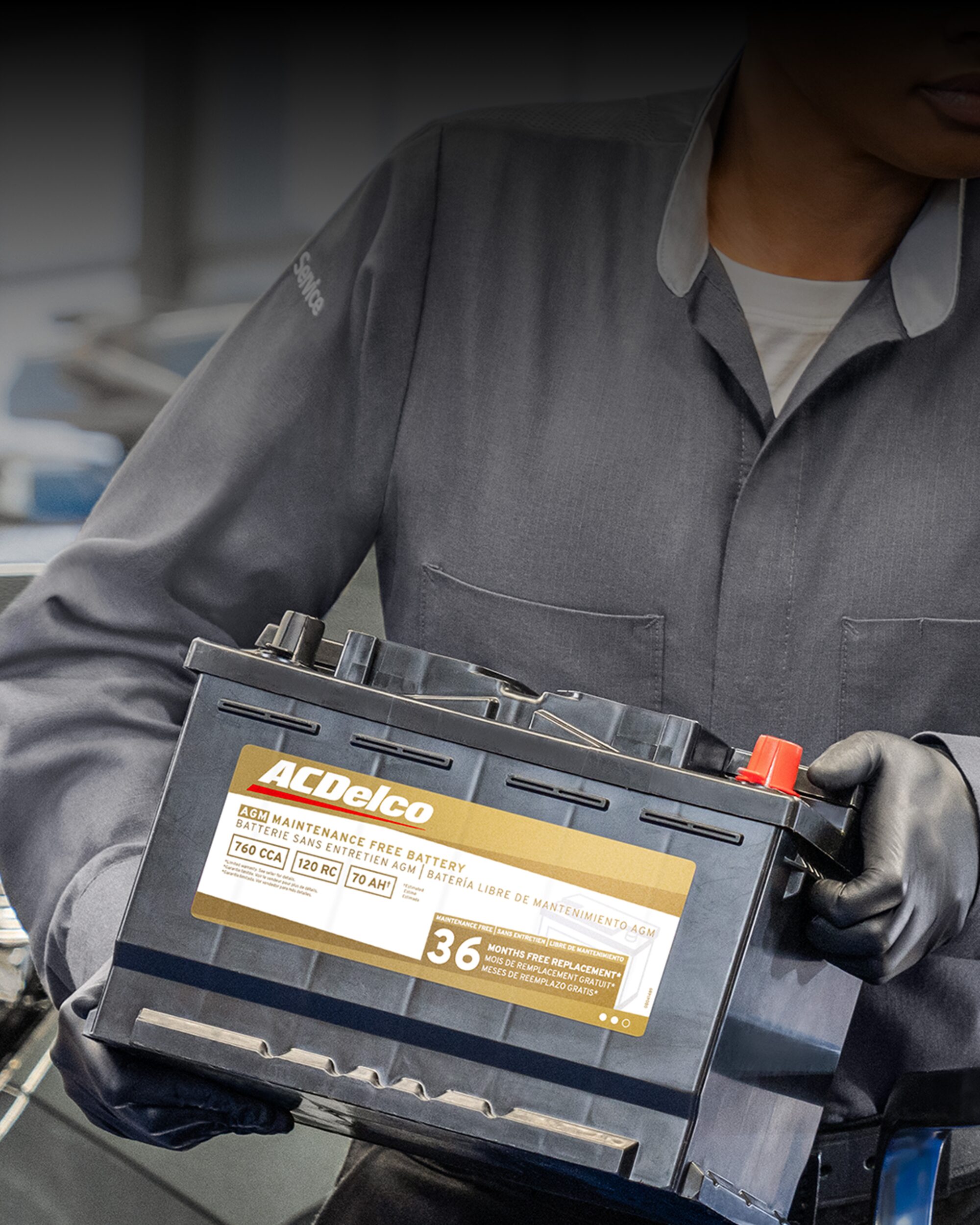 A Close-up View of a Service Technician Holding an ACDelco Battery While Standing in Front of a Vehicle.