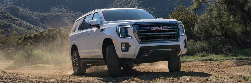 A GMC Yukon AT4 SUV Driving on a Dirt Path With Trees in the Background