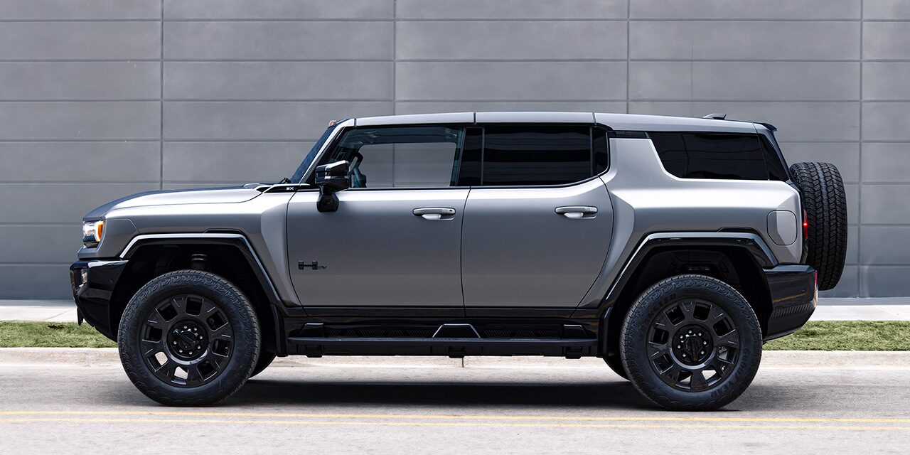 Front Three-Quarter View of the GMC HUMMER EV Pickup Truck Driving Down a Dirt Road with Mountains in the Background