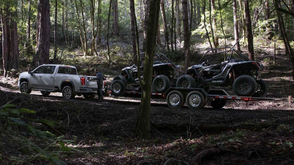 The Sierra HD Towing a Loaded Trailer Through a Woodsy Off-Road Trail