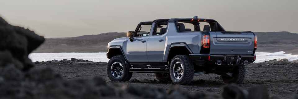 Rear Three-Quarters View of the 2025 Hummer EV Pickup Truck with the Top Off Parked on a Rocky Path