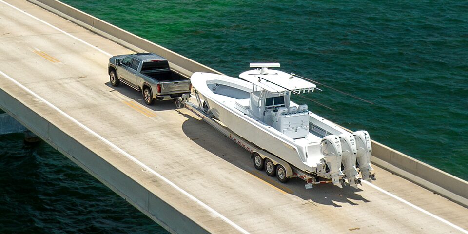 Wide Rear Three-Quarters Birdseye View of a 2025 GMC Sierra HD Hauling a Boat on an Open Road Near a Lake