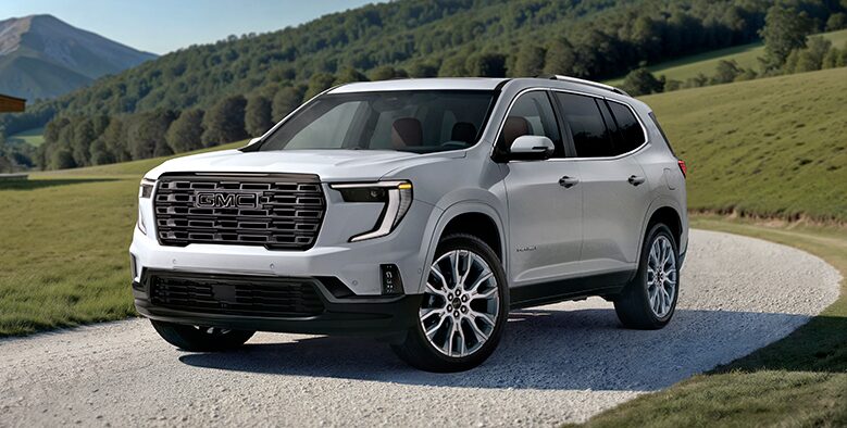 Front Three-Quarters View of a White 2026 GMC Acadia Mid-Size SUV Driving Down a Long Driveway